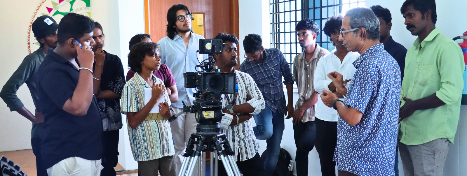A group of people gathered around a camera on a tripod, discussing filmmaking techniques in a preview theater setting.