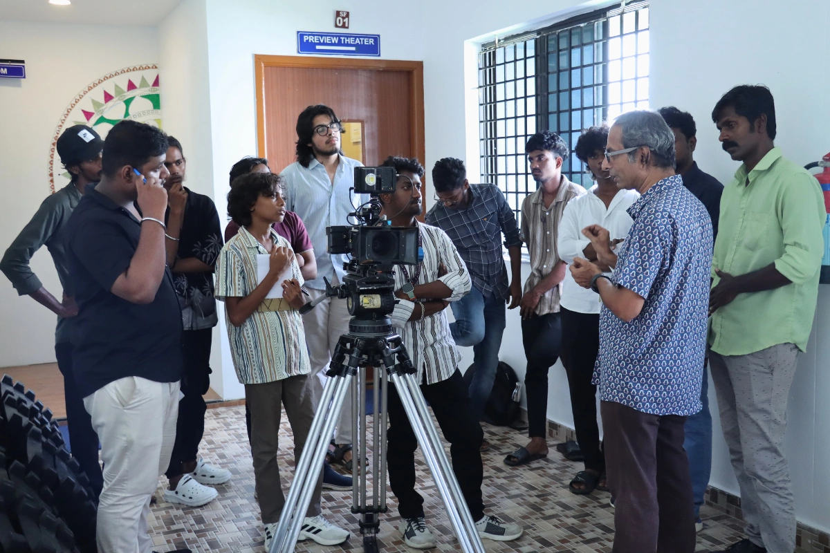 A group of people gathered around a camera on a tripod, discussing and observing in a room.