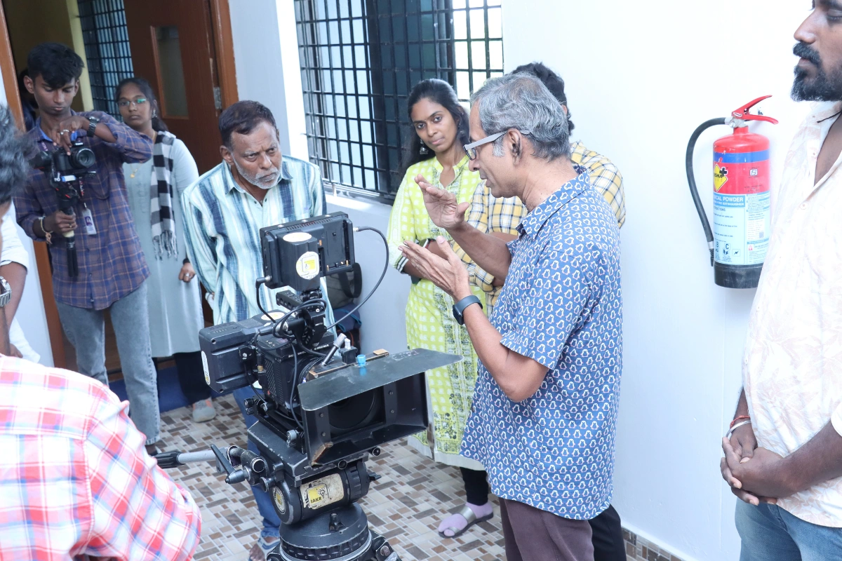 A group of filmmakers discussing techniques around a vintage camera in a well-lit studio setting, showcasing collaboration and creativity.
